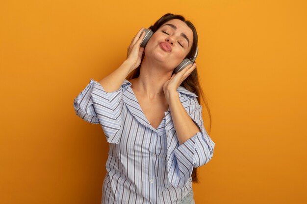 La bella donna soddisfatta sulle cuffie sta con gli occhi chiusi isolati sulla parete arancione