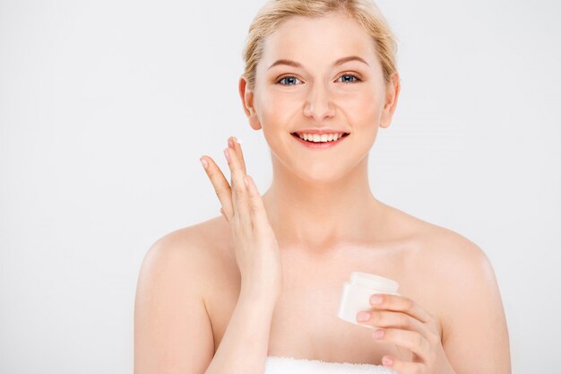 La bella donna sorridente applica la crema facciale