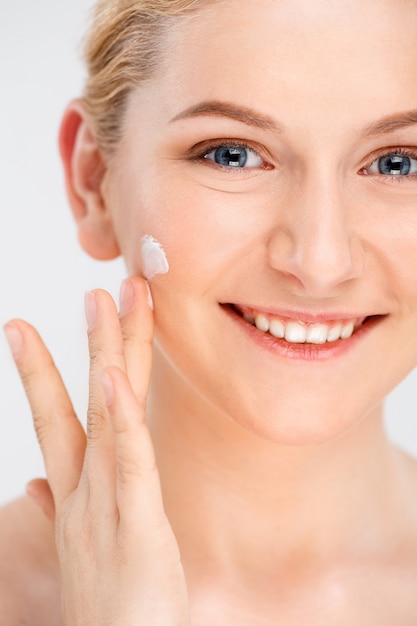 La bella donna sorridente applica la crema facciale