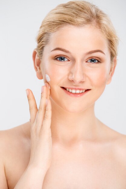 La bella donna sorridente applica la crema facciale