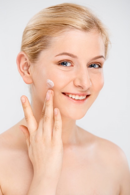 La bella donna sorridente applica la crema facciale