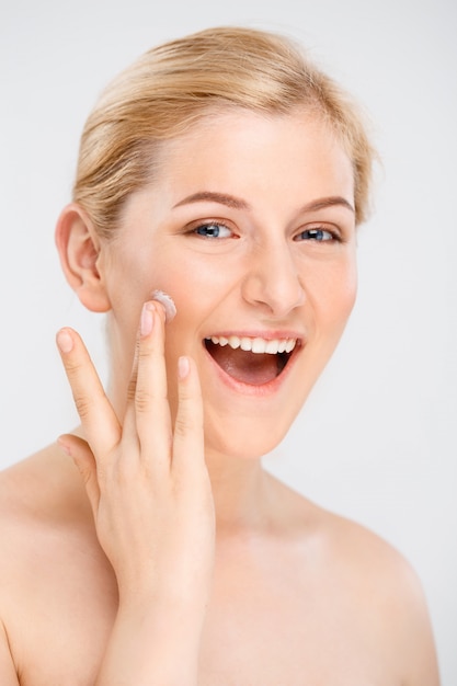 La bella donna sorridente applica la crema facciale