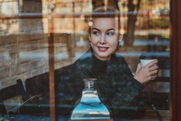 La bella donna sta godendo il suo caffè mentre si siede al caffè vicino alla finestra.