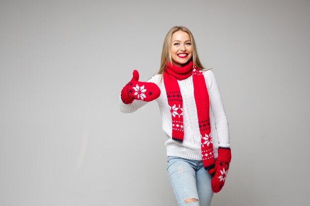 La bella femmina caucasica in maglione bianco, sciarpa rossa e guanti rossi ama qualcosa, immagine isolata su sfondo bianco