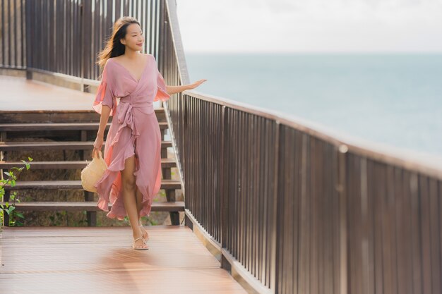 La bella giovane donna asiatica del ritratto che guarda l'oceano della spiaggia del mare per si rilassa nel viaggio di vacanza di festa