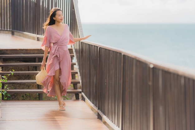 La bella giovane donna asiatica del ritratto che guarda l'oceano della spiaggia del mare per si rilassa nel viaggio di vacanza di festa