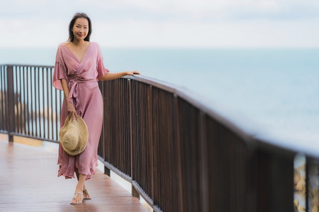 La bella giovane donna asiatica del ritratto che guarda l'oceano della spiaggia del mare per si rilassa nel viaggio di vacanza di festa