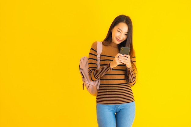 La bella giovane donna asiatica del ritratto con il bagpack utilizza lo smartphone