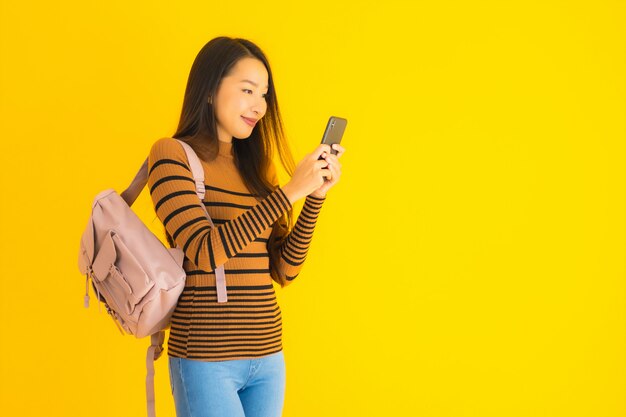 La bella giovane donna asiatica del ritratto con il bagpack utilizza lo smartphone