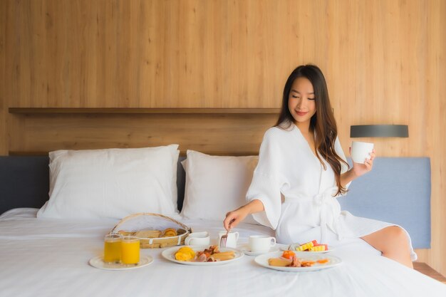 La bella giovane donna asiatica del ritratto felice gode di con la prima colazione sul letto in camera da letto