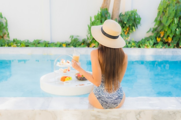 La bella giovane donna asiatica del ritratto gode di con il tè o la prima colazione di pomeriggio che galleggia sulla piscina