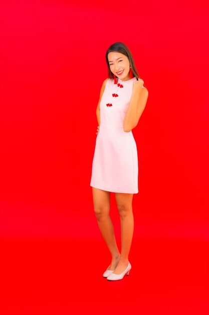 La bella giovane donna asiatica del ritratto indossa i vestiti cinesi del capodanno sulla parete rossa