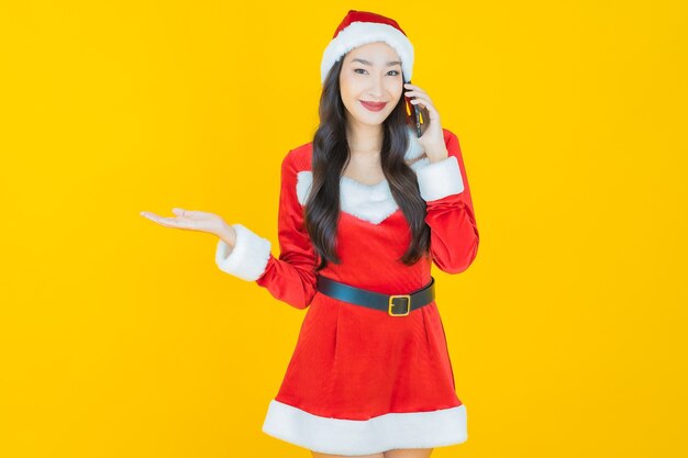 La bella giovane donna asiatica del ritratto indossa il costume di natale con il telefono cellulare su yellow