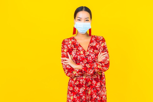 La bella giovane donna asiatica del ritratto indossa la maschera per proteggere il virus corona o covid19 sulla parete gialla