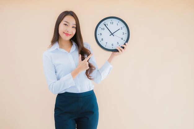 La bella giovane donna asiatica del ritratto mostra la sveglia o l'orologio