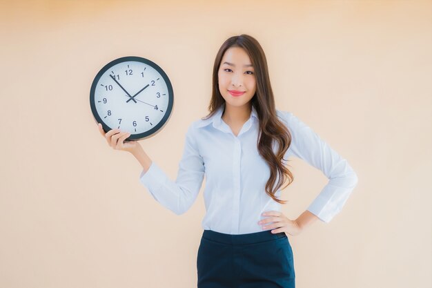 La bella giovane donna asiatica del ritratto mostra la sveglia o l'orologio