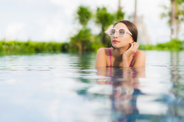 La bella giovane donna asiatica del ritratto si rilassa gode intorno alla piscina all'aperto nella vacanza di festa