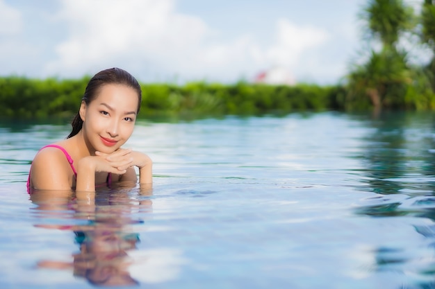 La bella giovane donna asiatica del ritratto si rilassa gode intorno alla piscina all'aperto nella vacanza di festa