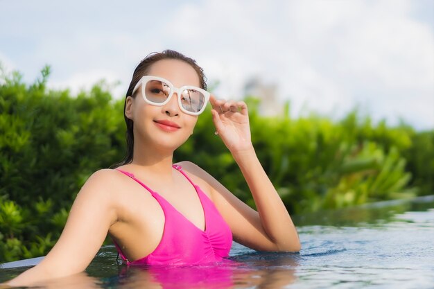 La bella giovane donna asiatica del ritratto si rilassa gode intorno alla piscina all'aperto nella vacanza di festa