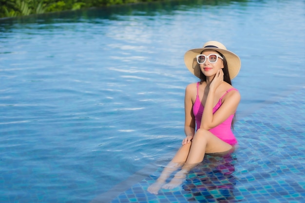 La bella giovane donna asiatica del ritratto si rilassa gode intorno alla piscina all'aperto nella vacanza di festa