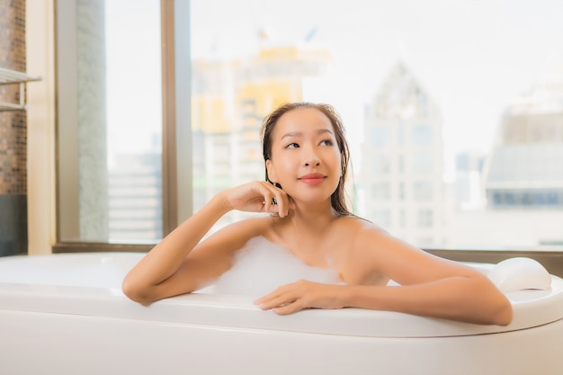 La bella giovane donna asiatica del ritratto si rilassa godere di fare un bagno nella vasca da bagno nell'interno del bagno