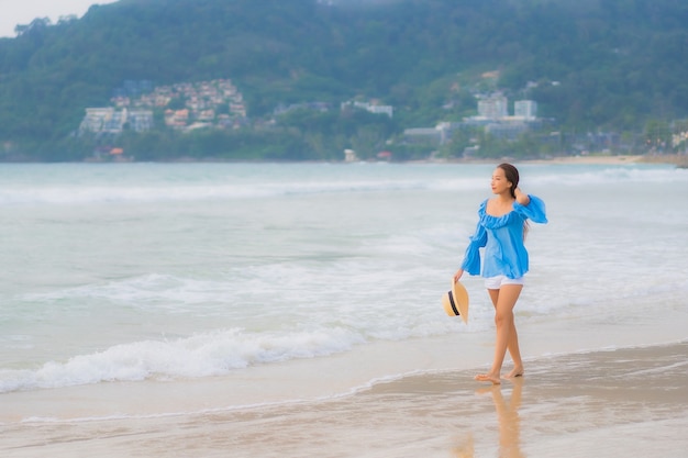 La bella giovane donna asiatica del ritratto si rilassa il sorriso di svago intorno all'oceano del mare della spiaggia all'ora del tramonto