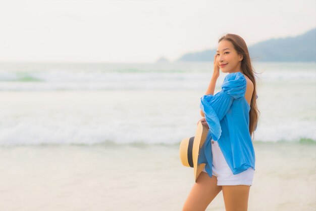 La bella giovane donna asiatica del ritratto si rilassa il sorriso di svago intorno all'oceano del mare della spiaggia all'ora del tramonto