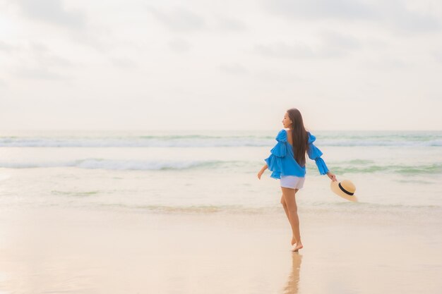 La bella giovane donna asiatica del ritratto si rilassa il sorriso di svago intorno all'oceano del mare della spiaggia all'ora del tramonto