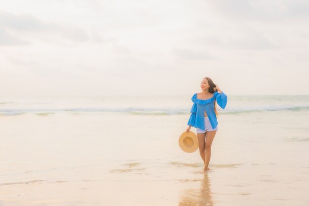 La bella giovane donna asiatica del ritratto si rilassa il sorriso di svago intorno all'oceano del mare della spiaggia all'ora del tramonto