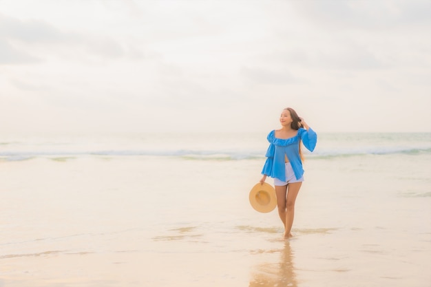 La bella giovane donna asiatica del ritratto si rilassa il sorriso di svago intorno all'oceano del mare della spiaggia all'ora del tramonto