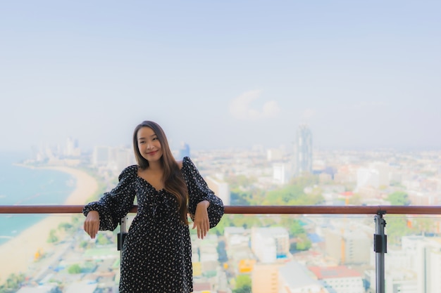 La bella giovane donna asiatica del ritratto si rilassa il sorriso felice intorno al balcone con la vista della città di Pattaya