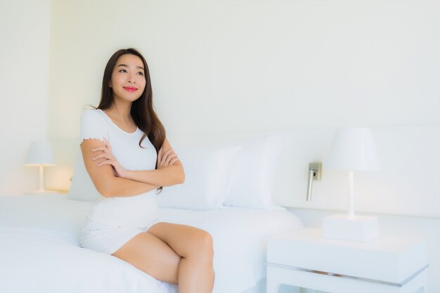 La bella giovane donna asiatica del ritratto si rilassa il sorriso felice sul letto con la coperta di cuscino bianca