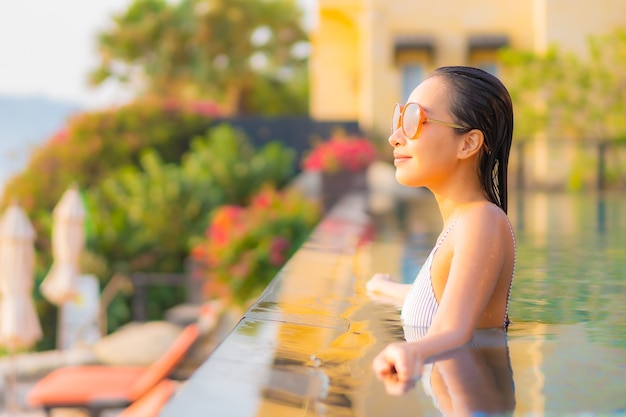 La bella giovane donna asiatica del ritratto si rilassa il sorriso gode del tempo libero intorno alla piscina nell'hotel della località di soggiorno in vacanza