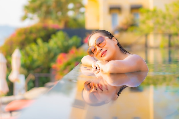 La bella giovane donna asiatica del ritratto si rilassa il sorriso gode del tempo libero intorno alla piscina nell'hotel della località di soggiorno in vacanza