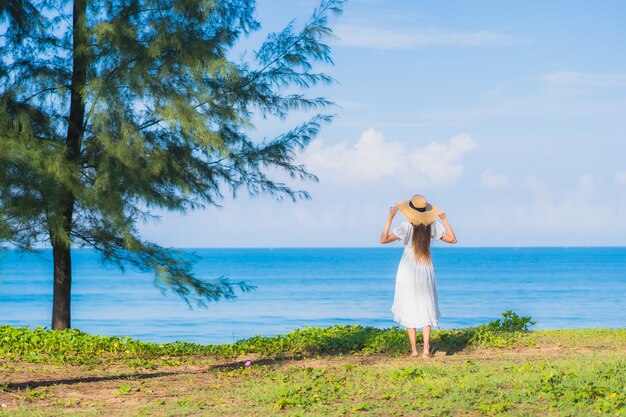 La bella giovane donna asiatica del ritratto si rilassa il sorriso intorno all'oceano del mare della spiaggia con la nuvola bianca del cielo blu per le vacanze di viaggio