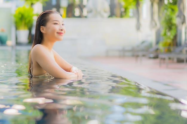 La bella giovane donna asiatica del ritratto si rilassa il sorriso intorno alla piscina all'aperto nella località di soggiorno dell'hotel sul viaggio di vacanza