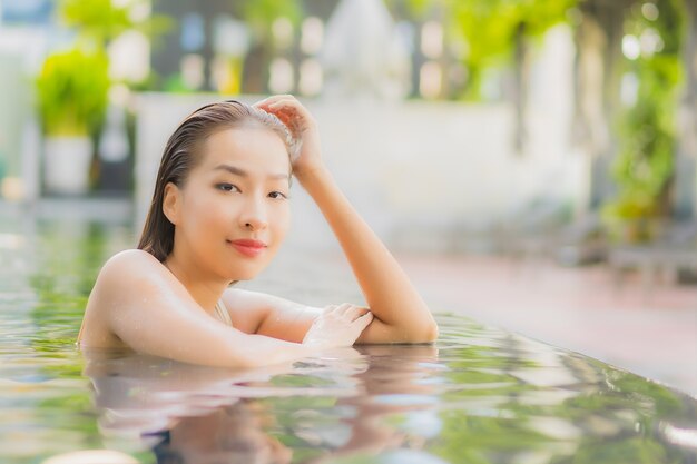 La bella giovane donna asiatica del ritratto si rilassa il sorriso intorno alla piscina all'aperto nella località di soggiorno dell'hotel sul viaggio di vacanza