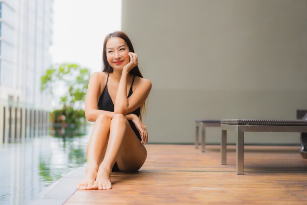 La bella giovane donna asiatica del ritratto si rilassa il sorriso intorno alla piscina all'aperto nella località di soggiorno dell'hotel