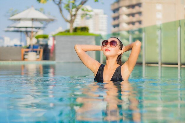 La bella giovane donna asiatica del ritratto si rilassa il sorriso intorno alla piscina all'aperto nella località di soggiorno dell'hotel