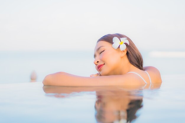 La bella giovane donna asiatica del ritratto si rilassa il sorriso intorno alla piscina all'aperto nella località di soggiorno dell'hotel