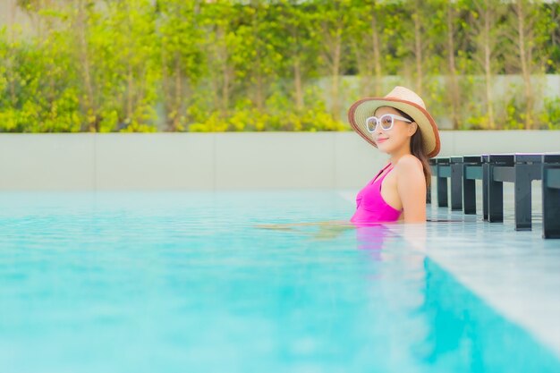 La bella giovane donna asiatica del ritratto si rilassa il sorriso intorno alla piscina all'aperto nella località di soggiorno dell'hotel