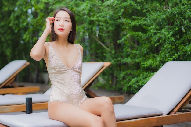 La bella giovane donna asiatica del ritratto si rilassa il sorriso intorno alla piscina all'aperto