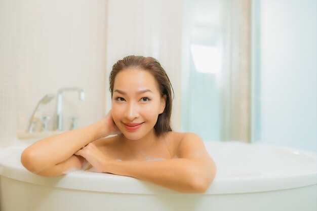 La bella giovane donna asiatica del ritratto si rilassa il sorriso nella vasca da bagno all'interno del bagno