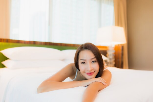 La bella giovane donna asiatica del ritratto si rilassa il sorriso sul letto nell'interno della camera da letto