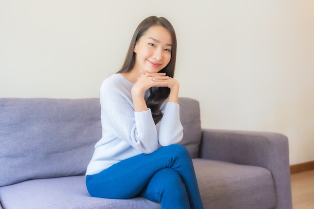 La bella giovane donna asiatica del ritratto si rilassa il sorriso sul sofà in soggiorno