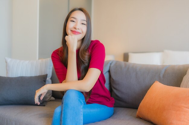 La bella giovane donna asiatica del ritratto si rilassa il sorriso sul sofà nella zona vivente