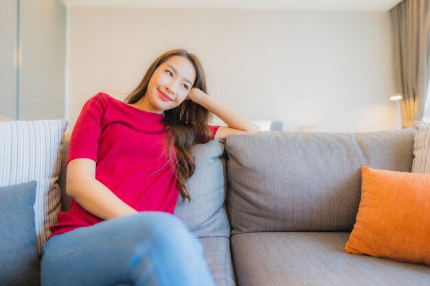 La bella giovane donna asiatica del ritratto si rilassa il sorriso sul sofà nella zona vivente