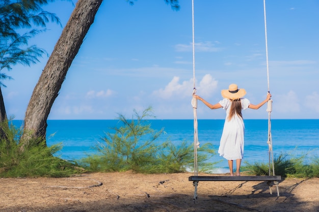 La bella giovane donna asiatica del ritratto si rilassa il sorriso sull'oscillazione intorno all'oceano del mare della spiaggia per il viaggio della natura in vacanza