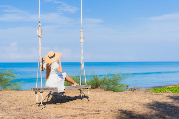 La bella giovane donna asiatica del ritratto si rilassa il sorriso sull'oscillazione intorno all'oceano del mare della spiaggia per il viaggio della natura in vacanza