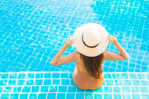 La bella giovane donna asiatica del ritratto si rilassa il tempo libero di sorriso intorno alla piscina all'aperto con la vista dell'oceano del mare